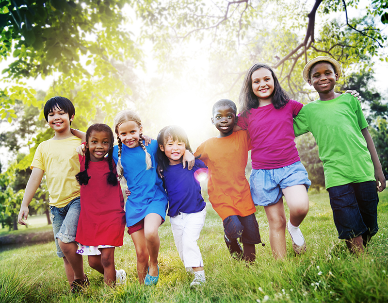 7 children walking through the grass towards the the camera with the sun behind them
